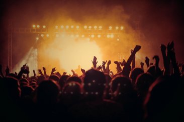 Menschenmenge hebt die Hände bei einem Konzert mit Bühnenlichtern