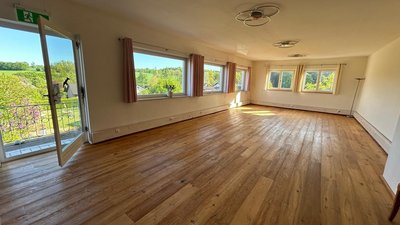 Großer, leerer Raum mit Holzboden und Fensterblick nach draußen