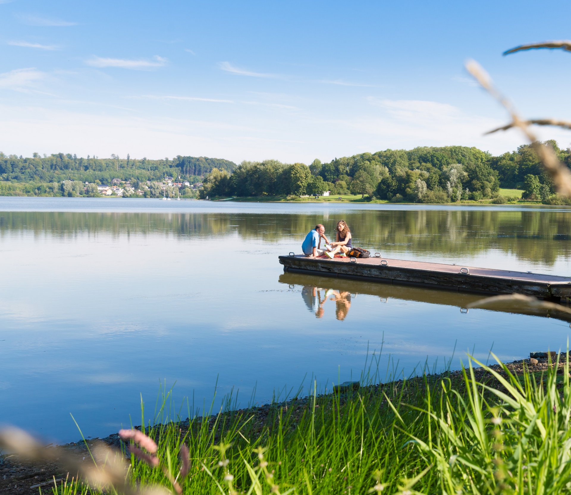 Zwei Personen sitzen auf einem Holzsteg am See, Fahrrad daneben