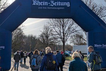 Besucher gehen unter einem blauen Bogen der Rhein-Zeitung in einen Park