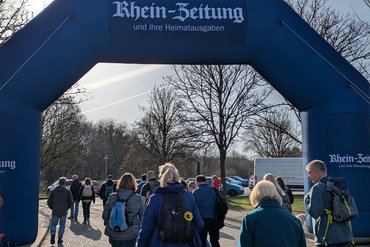 Besucher gehen unter einem blauen Bogen der Rhein-Zeitung in einen Park