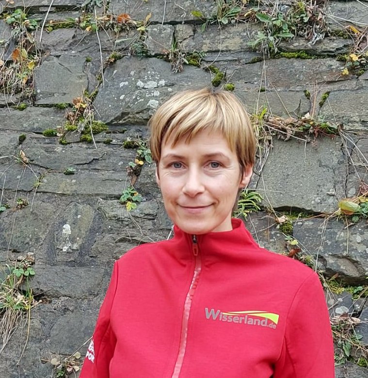 Wanderführerin in rotem Outfit vor einer Steinmauer