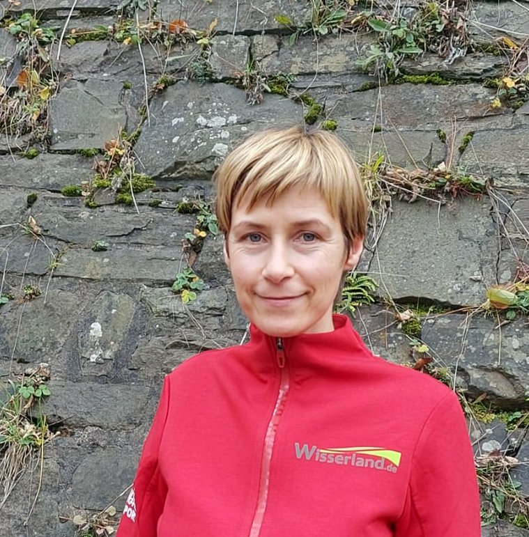 Wanderführerin in rotem Outfit vor einer Steinmauer