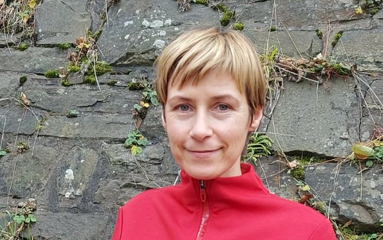 Wanderführerin in rotem Outfit vor einer Steinmauer