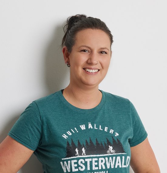 Frau posiert lächelnd an einer Wand in einem grünen T-Shirt