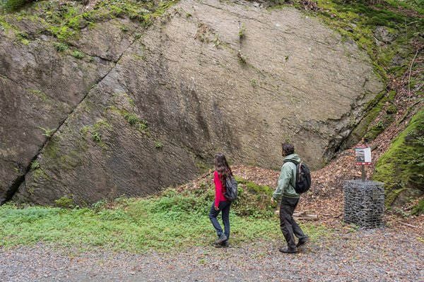 Zwei Personen gehen an einer rauen Felswand entlang in der Natur