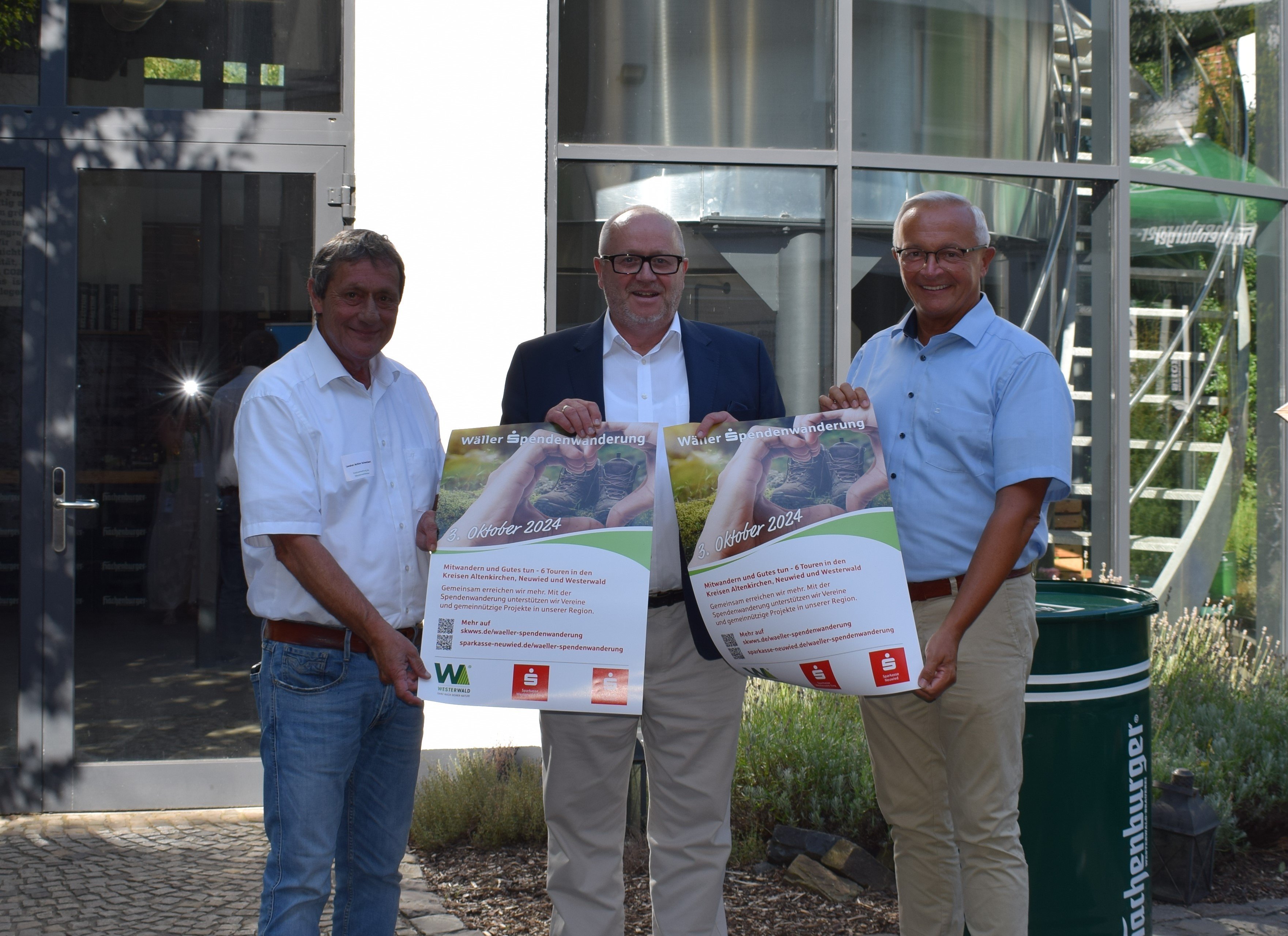 Drei Personen präsentieren Poster zur Veranstaltung im Freien.