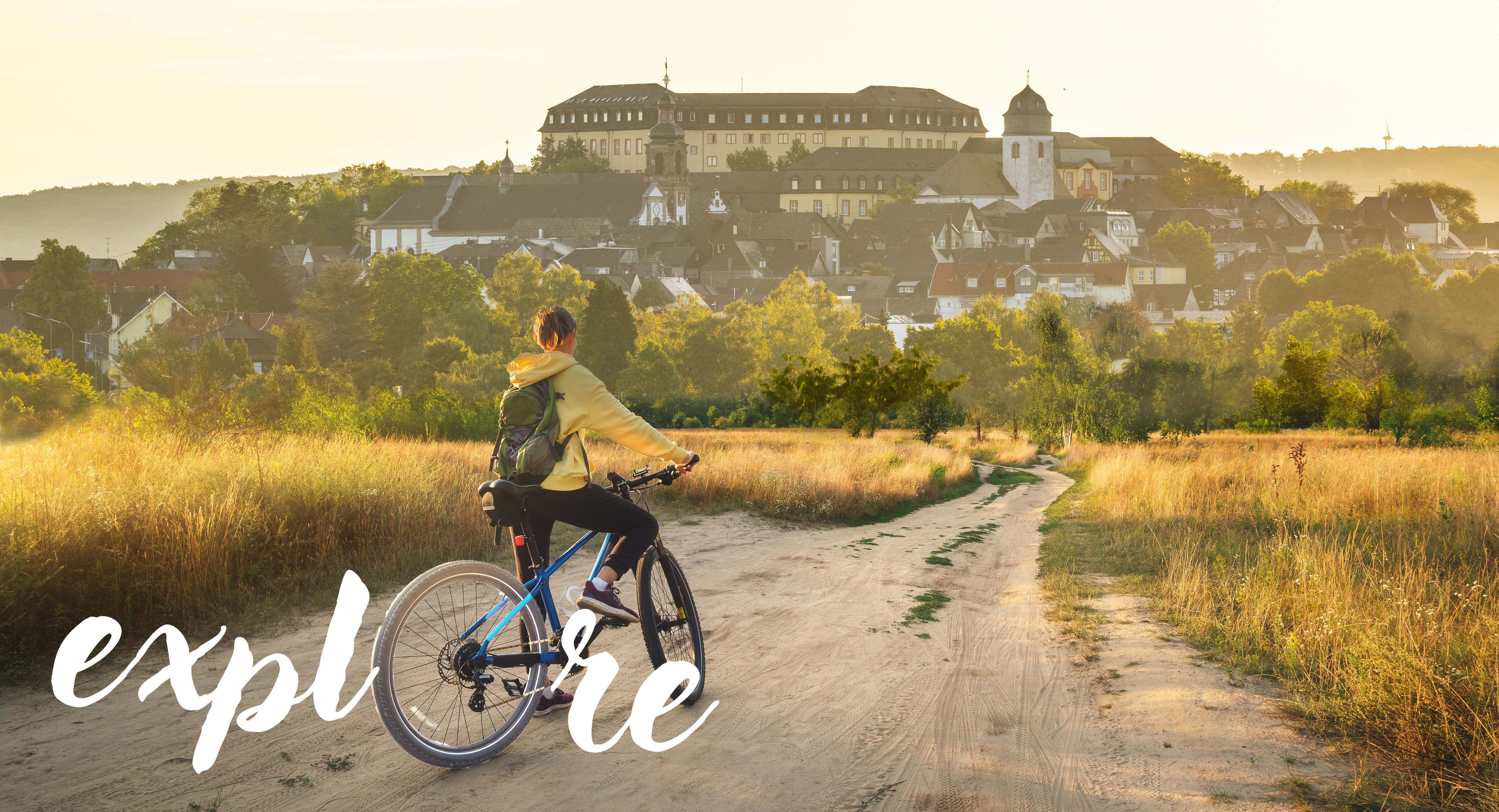 A cyclist on a dirt road with a village in the background in golden light.
