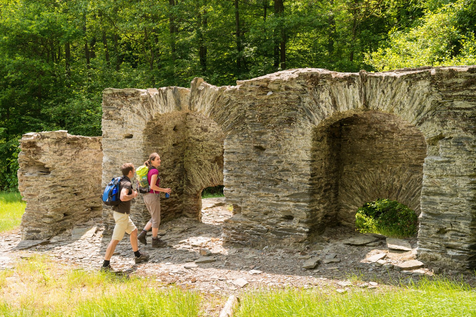 Zwei Personen erkunden alte Steinruinen umgeben von Bäumen