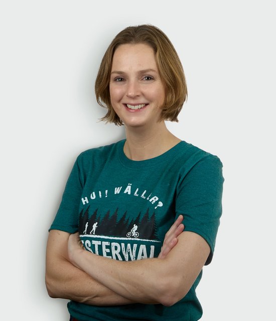 Frau mit hochgestecktem Haar in einem grünen T-Shirt, lächelnd und mit verschränkten Armen