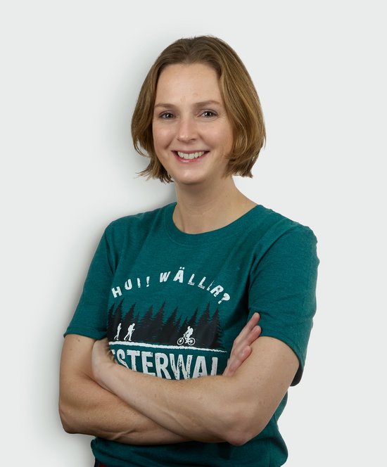 Frau mit hochgestecktem Haar in einem grünen T-Shirt, lächelnd und mit verschränkten Armen