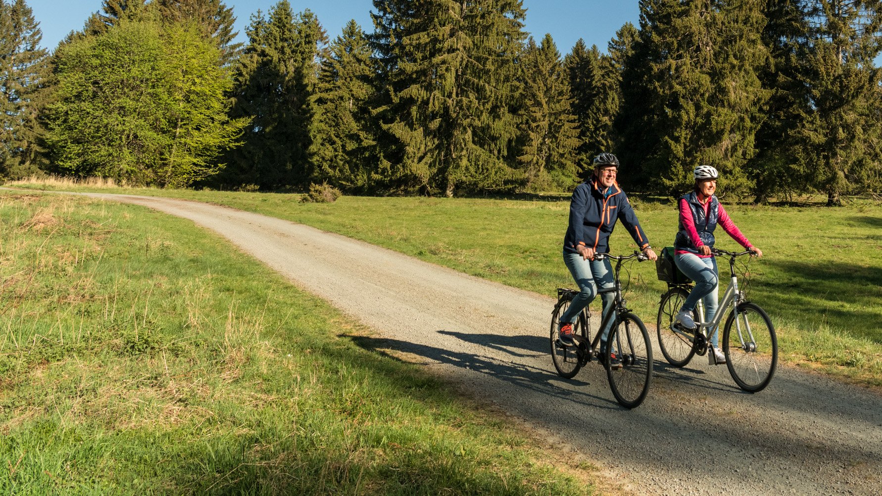 Zwei Frauen fahren mit Fahrrädern auf einem Waldweg bei klarem Himmel