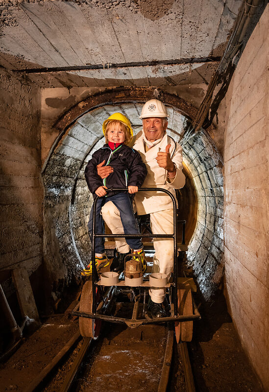 Ein Mann und ein Kind lächeln auf einem Schienenfahrzeug im Tunnel
