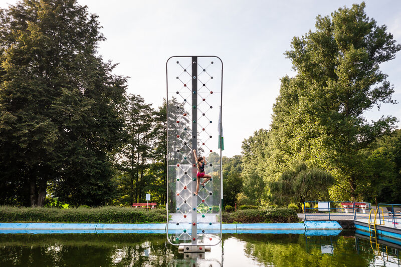 Junge klettert an Kletterwand über Wasserfläche im Park